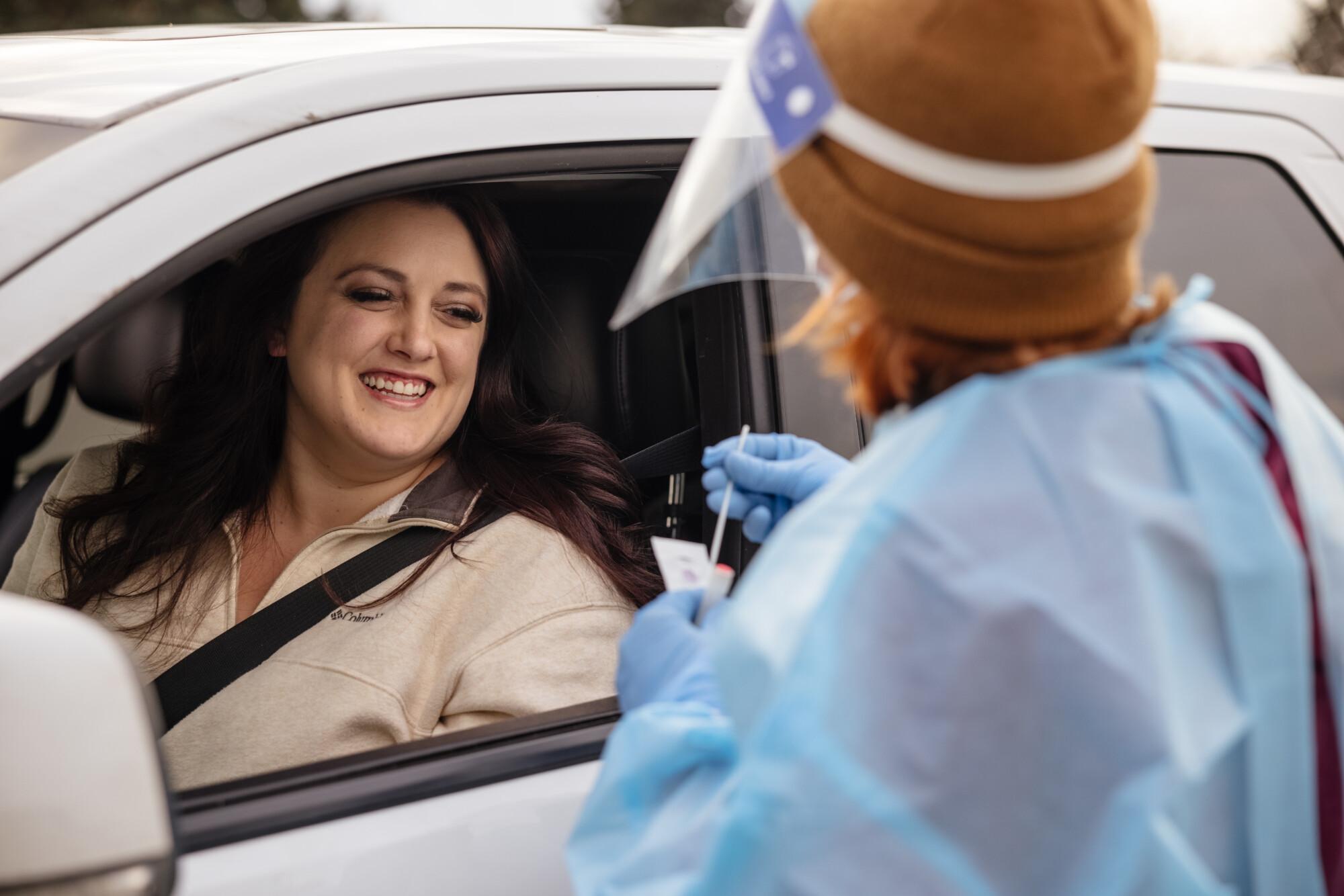 Image of smiling woman in car and Covid testing employee at a drive up testing site